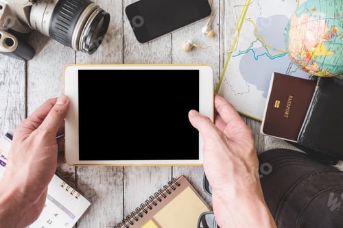 Preview: Top view of Male hands holding tablet with travel equipment on white wooden table background