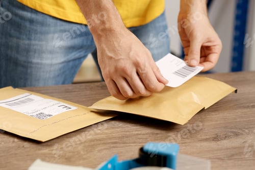 Preview: Post office worker sticking barcode on parcel at counter indoors, closeup