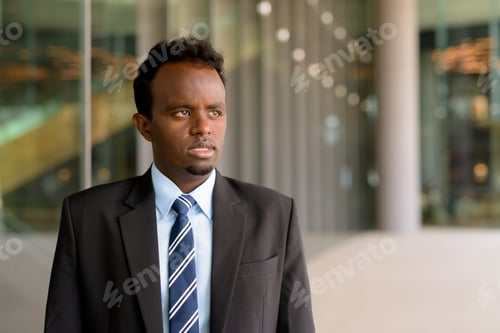 Preview: Portrait of African businessman wearing suit and tie outdoors in city while thinking