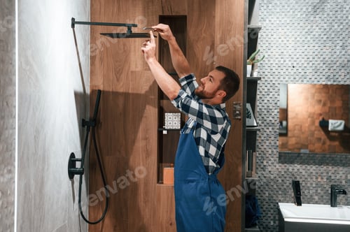 Preview: Repairs the shower faucet. Plumber in blue uniform is at work in the bathroom