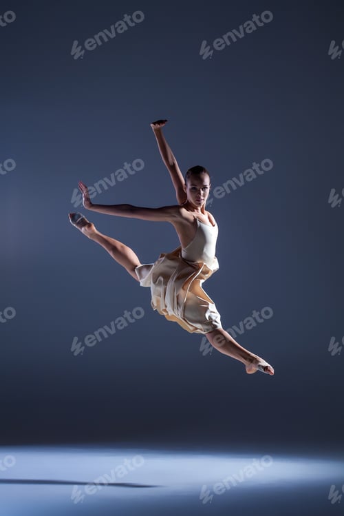 Preview: Young beautiful dancer in beige dress jumping on gray background