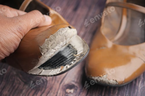 Preview: Worn shoes held by a hand show signs of damage and use