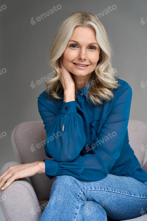 Preview: Smiling 50s middle aged woman model sitting in chair looking at camera.