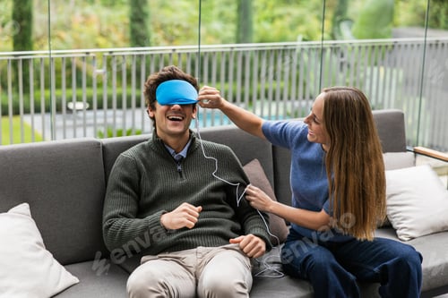 Preview: Couple relaxing on sofa, woman placing sleep mask on man