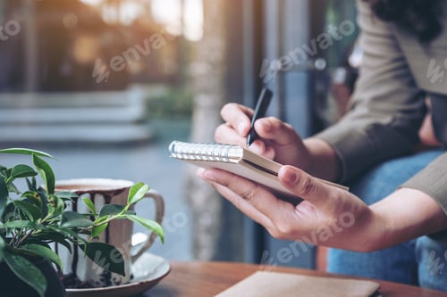 Preview: a woman's hands holding and writing on blank notebook with coffee cup on wooden table