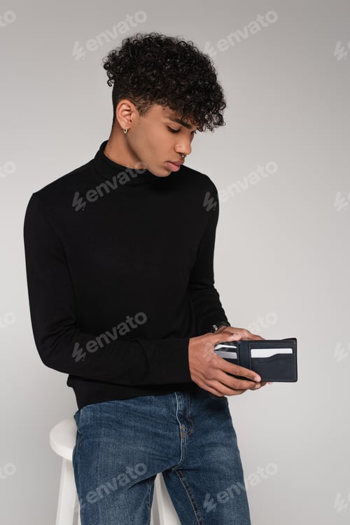 Preview: young african american man looking inside of leather wallet isolated on grey