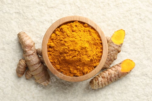 Preview: Turmeric powder in bowl and roots on light textured table, flat lay