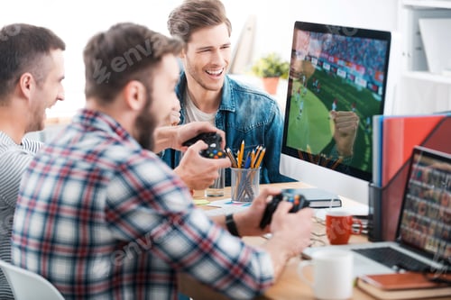 Preview: Testing new game. Three young men playing computer games while sitting at the desk in the office