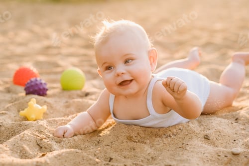 Preview: A happy little boy is lying on a sandy beach near the sea in the rays of the setting sun