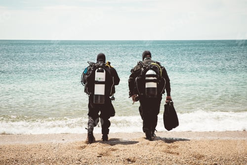Preview: Two deep sea divers wearing wetsuits and oxygen bottles walking into the ocean from a beach