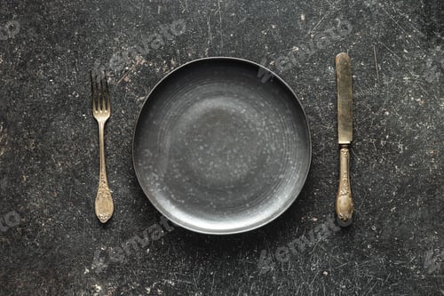 Preview: Empty vintage plate with silver knife and fork on black table.