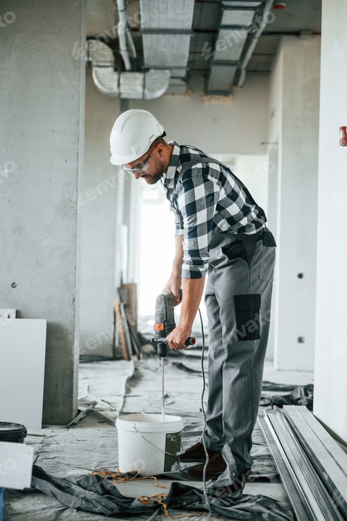 Preview: With drill. Repairman in uniform is in the unfinished building