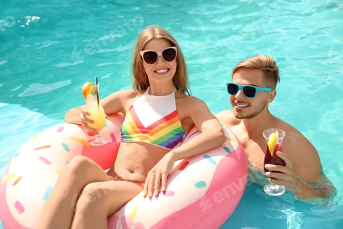Preview: Young couple with cocktails in pool on sunny day