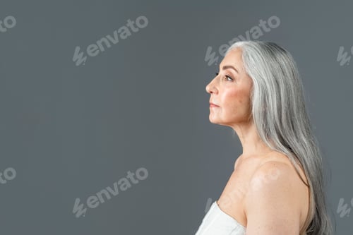 Preview: Serious retired european lady with gray hair look at copy space, isolated on gray background, studio