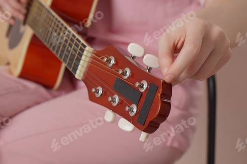 Preview: Extreme close-up woman's hands tuning six string acoustic guitar, tightening and loosening string