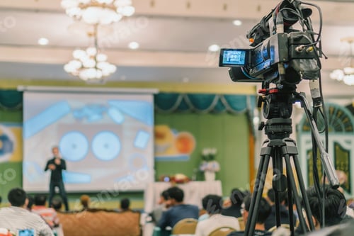 Preview: Rear side of Video Cameraman taking photograph to Asian Speaker with casual suit on the stage