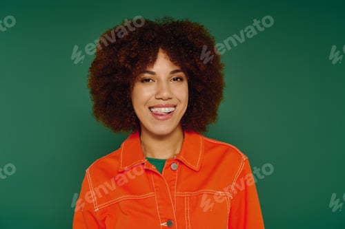 Preview: Young woman with curly hair expresses joy in casual attire against a vibrant green backdrop