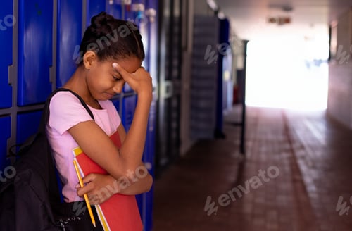 Preview: African American student standing in school hallway, with red binder and pencils, looking worried