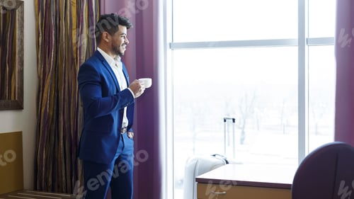 Preview: Handsome man in suit drinking coffee near window in hotel