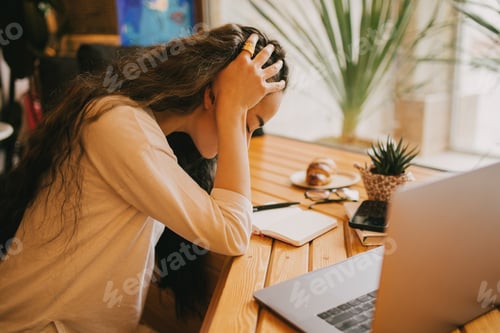 Preview: Tired exhausted woman freelancer working online using laptop and notebook, sitting in a coffeehouse.