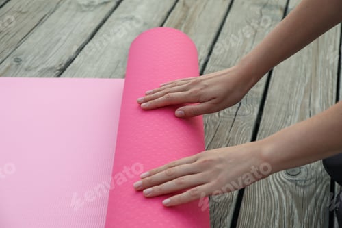 Preview: Pink yoga mat and female hands on wooden background, close up