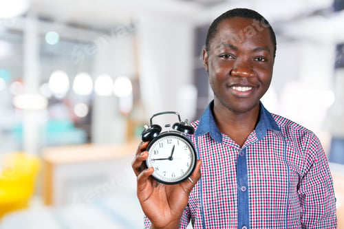 Preview: Man holding clock in a bright office space while smiling and looking at the camera