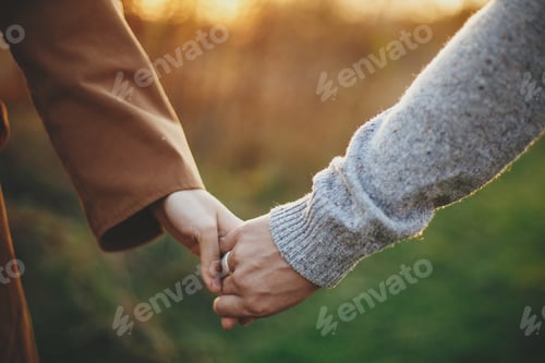 Preview: Couple gently holding hands in warm sunset light in autumn field, close up. Conceptual image