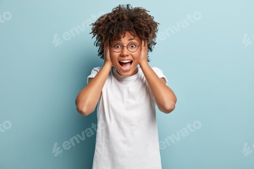 Preview: Photo of impressed overemotive woman with dark healthy skin, keeps both hands on head, looks joyfull