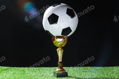 Preview: Soccer trophy with ball placed on grass against dark background during a sports event