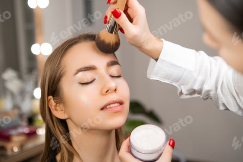 Preview: Cosmetologist applies powder with a brush to a fair-haired woman.