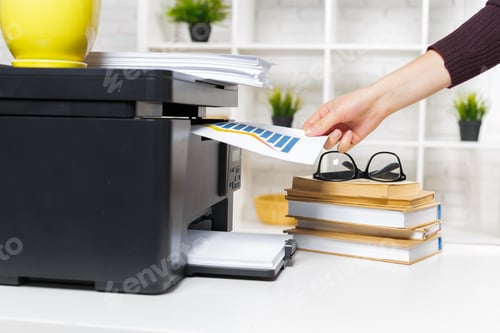 Preview: Hand inserting paper into printer in home office with books and glasses nearby