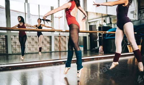 Preview: Crop women in bodysuits jumping on pointe above floor in studio training ballet.