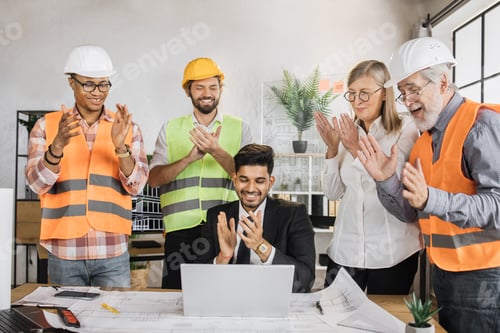 Preview: Team of engineers rejoices clapping their hands looking at laptop after a successful project.