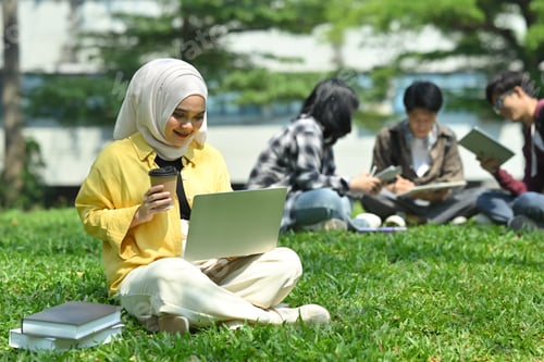 Preview: Happy young muslim student using laptop on green meadow in campus.