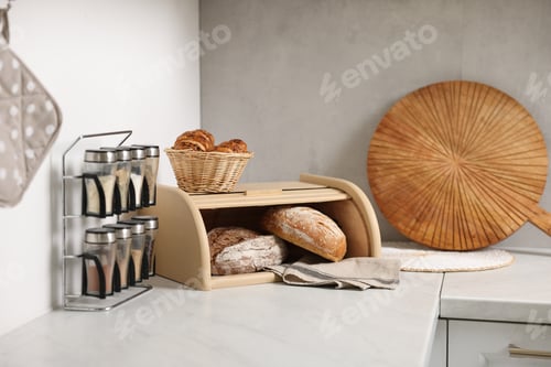 Preview: Wooden bread basket, freshly baked loaves and croissants on white marble table in kitchen