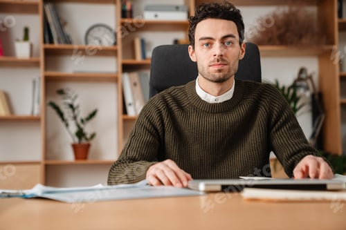 Preview: Man Wearing Sweater Sits at Desk in Office