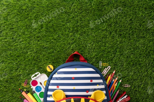 Preview: School backpack with various supplies on green grass background, signifying back to school season