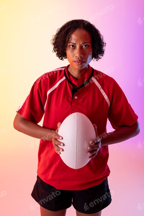 Preview: Portrait of african american female rugby player with rugby ball over neon pink lighting