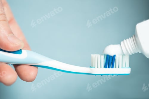 Preview: Person holding a blue toothbrush with a paste on blue background-Health concept
