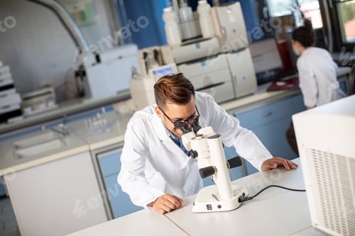 Preview: Young scientist in white lab coat working with binocular microscope in the material science lab