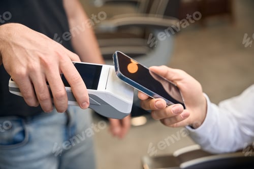Preview: Male client making contactless paying with smartphone on pos terminal
