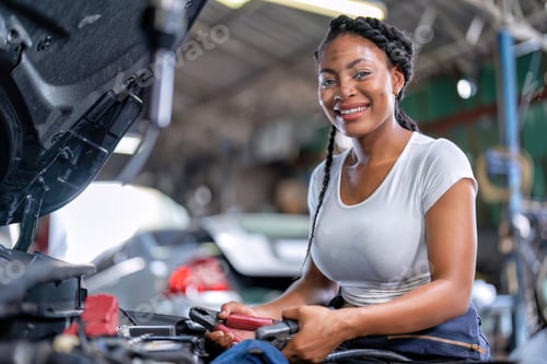 Preview: Mechanical girl at car repair shop stand hold battery jumper
