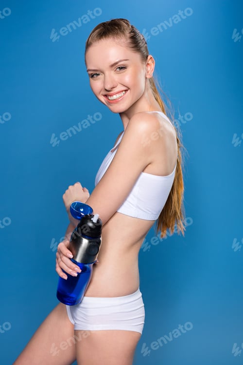 Preview: young sportswoman holding sport bottle with water isolated on blue