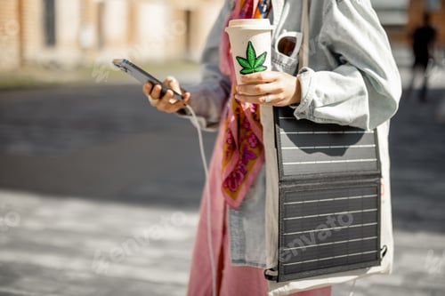 Preview: Woman charge phone from portable solar panel while walking outdoors