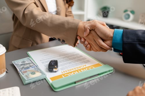 Preview: A car sales representative and a customer shake hands after signing a vehicle purchase contract.