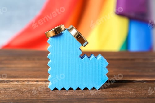 Preview: Heart figure with wedding rings and rainbow flag on background. Gay marriage