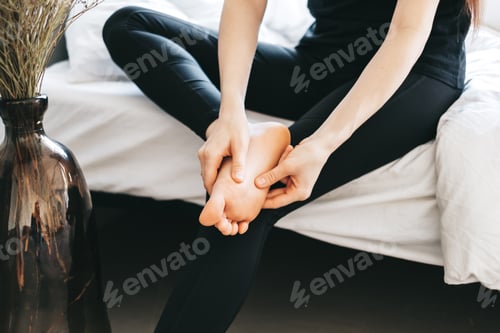 Preview: Young woman massaging her foot on the white bed after training or hard working day.
