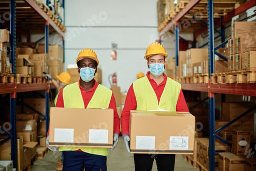 Preview: Multiracial warehouse workers holding delivery boxes while wearing safety mask