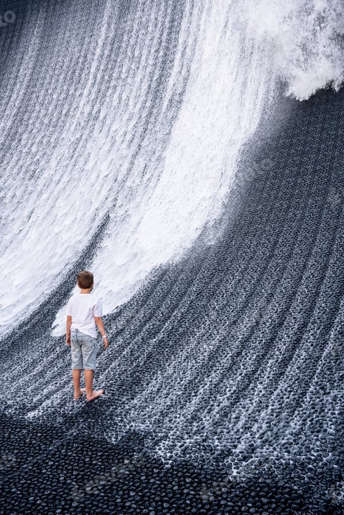 Preview: A boy in denim shorts and a white T-shirt looks at an artificial waterfall.