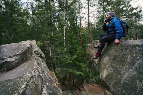 Preview: Foot traveller taking phone call on rock in forest